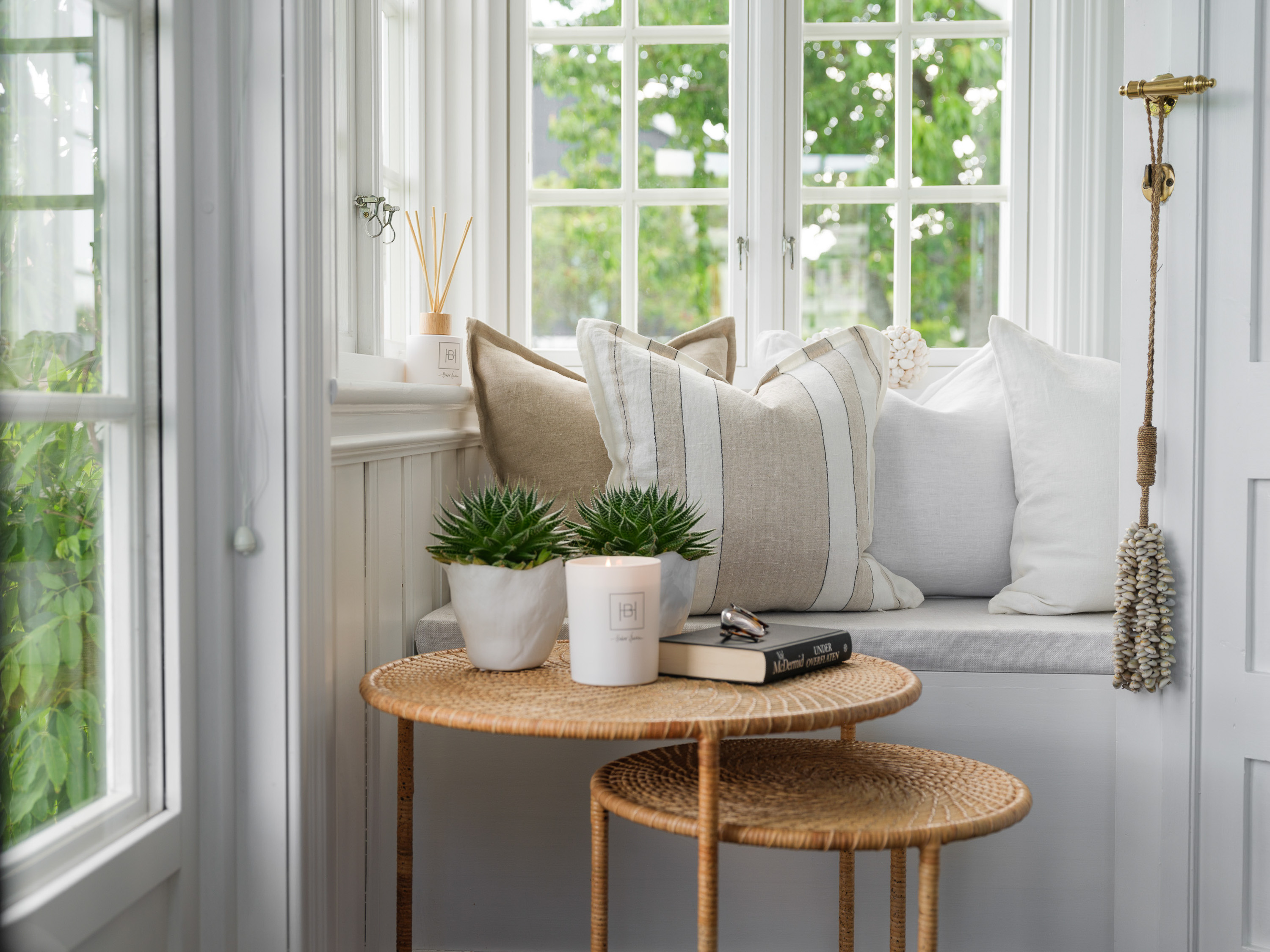 koselig hjørne i rom, med vinduer, to runde bord og flere puter på en polstret benk.