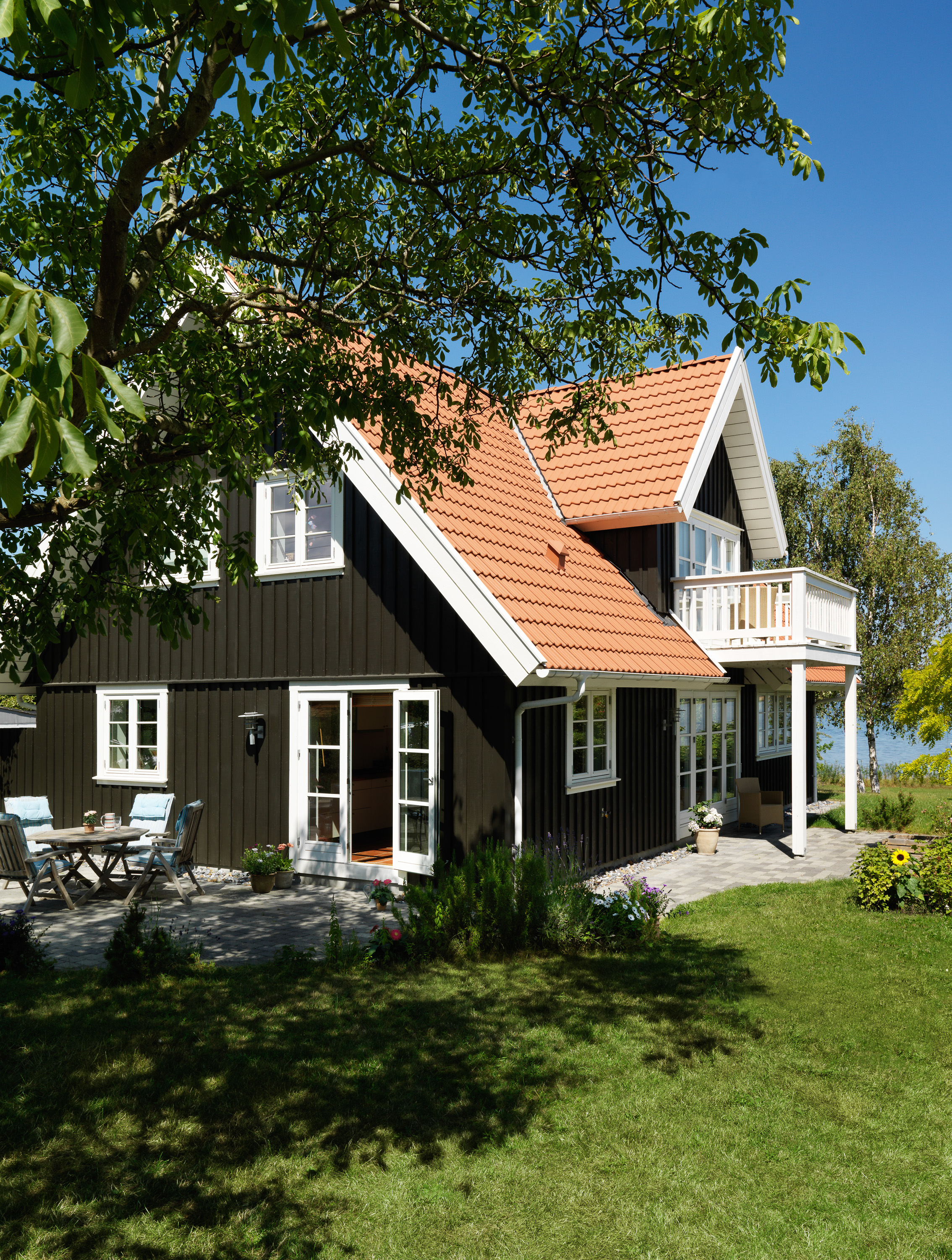 sort hus med rødt tegltak i en vårlig, grønn hage