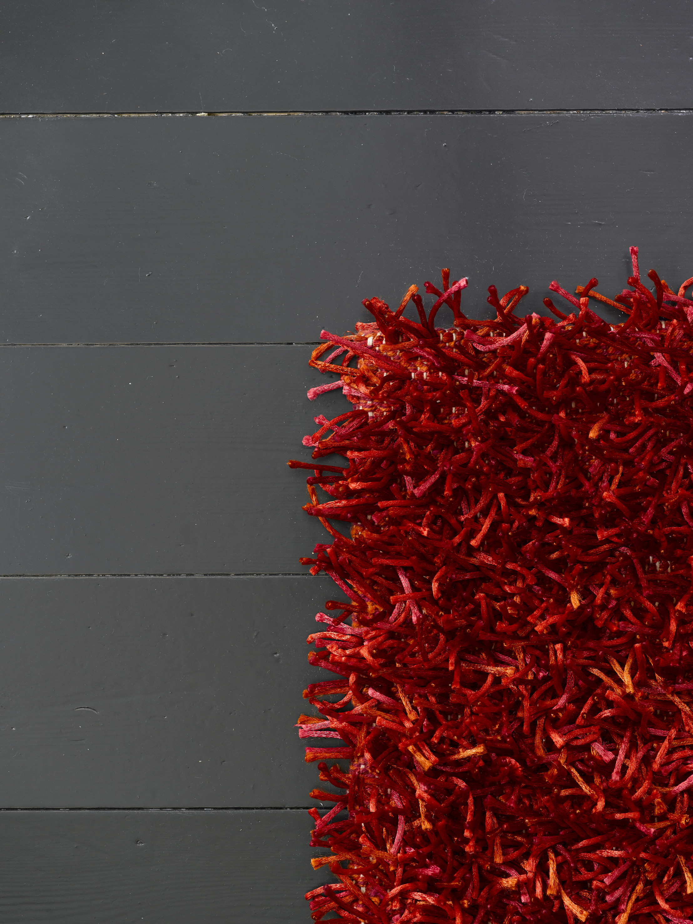 Rødt og grått – tøft teppe mot lekkert, blankt, nymalt gulv, med en farge som gir rommet tyngde og glans som sprer lyset. 